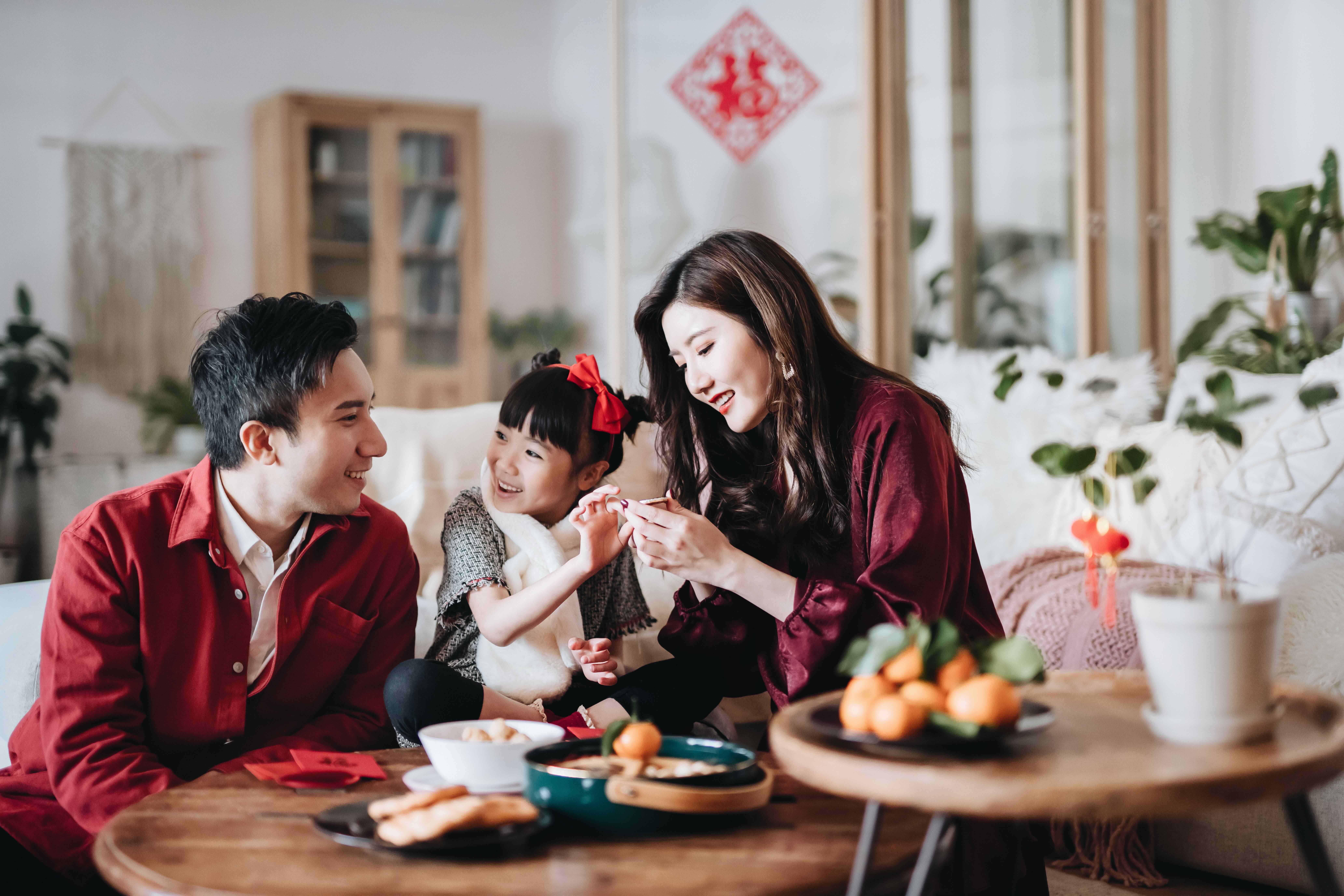 Lovely daughter chatting joyfully with father and mother and enjoying family bonding time while celebrating Chinese New Year at home
